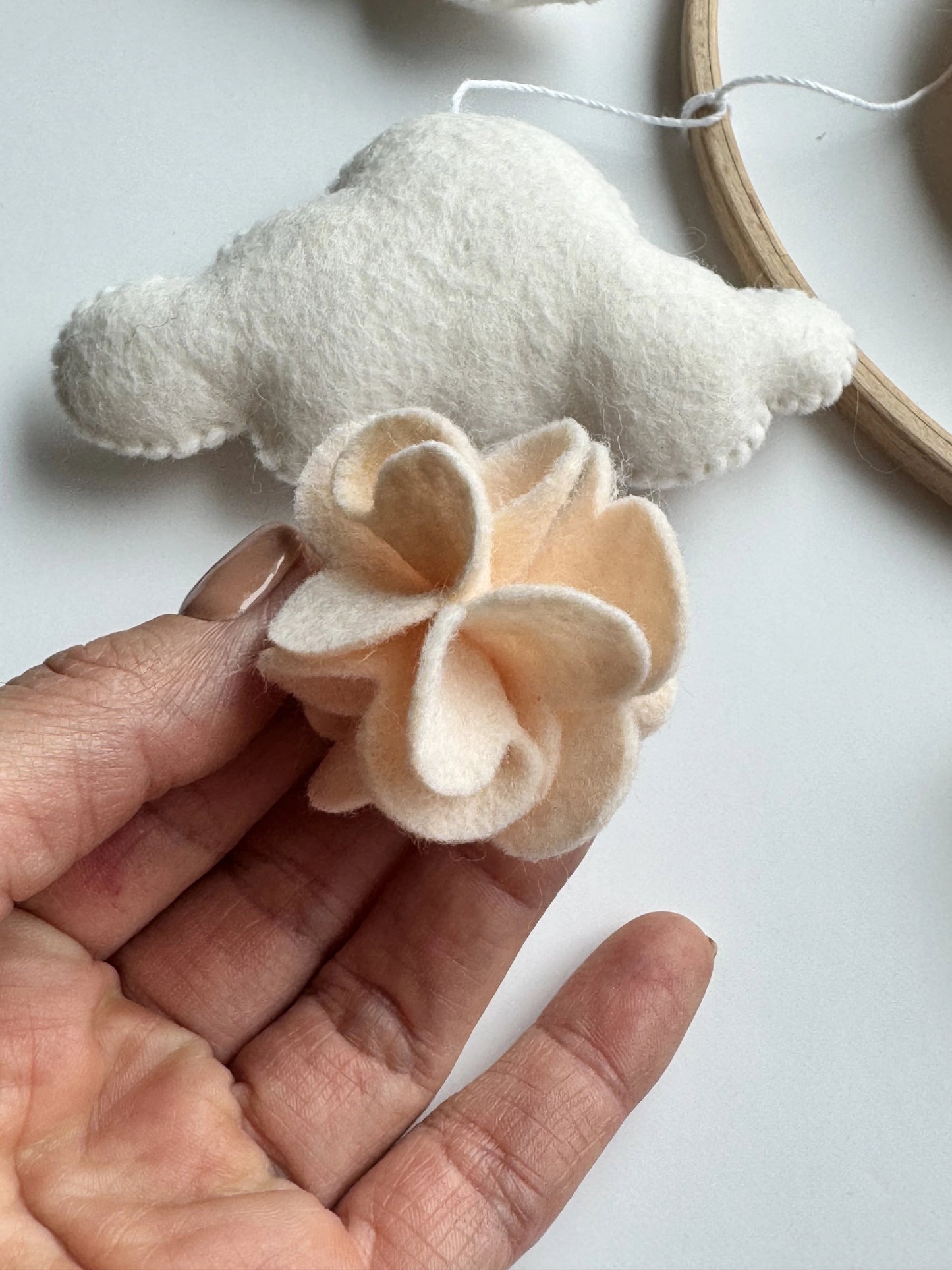 Hand holding a beige felt flower with a white cloud toy in the background